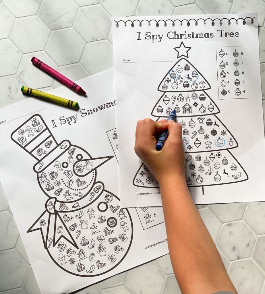 A child's hand holding a crayon, circling the I Spy items on the worksheets. 