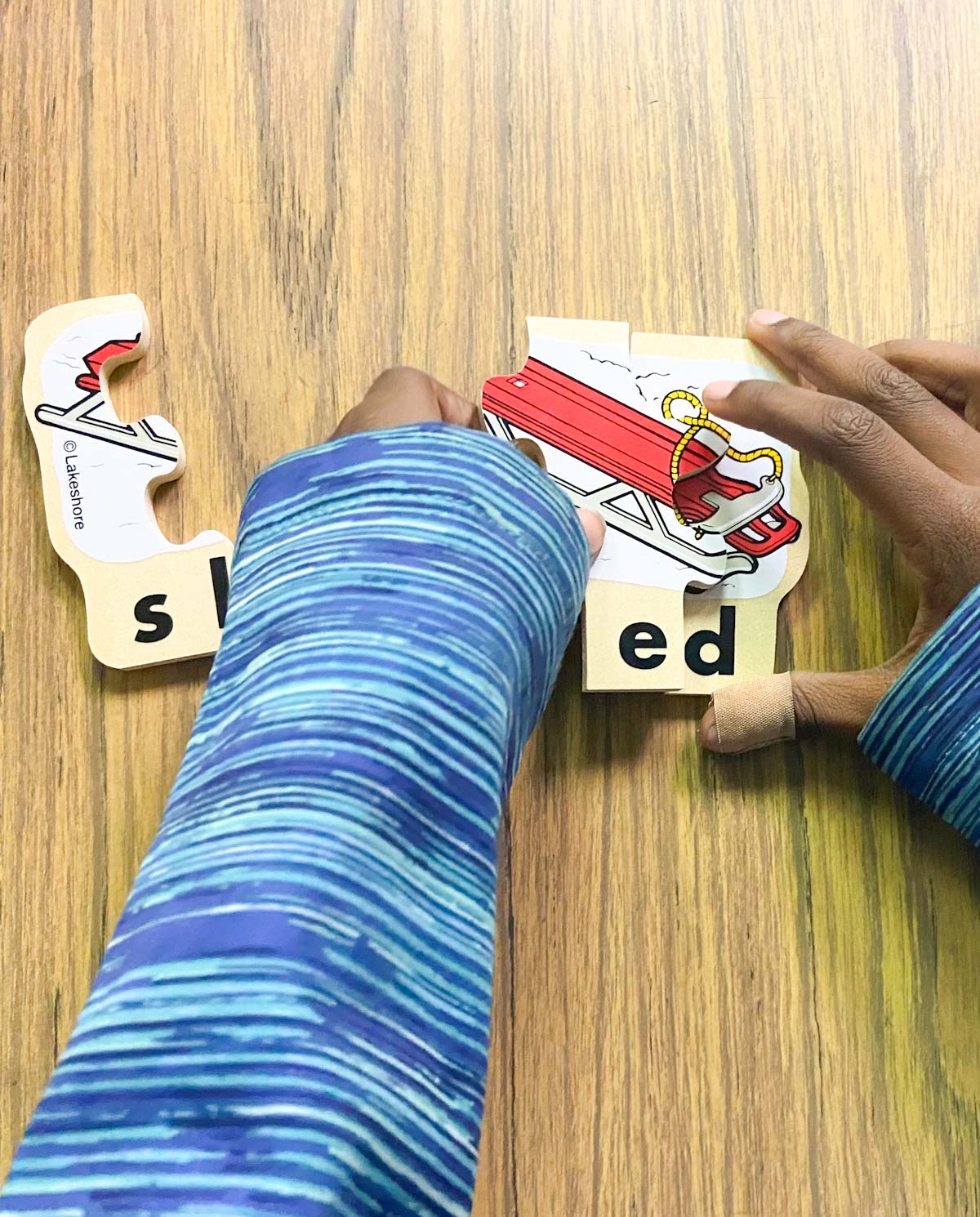 A child's hands putting together a small puzzle to create the word, "sled."