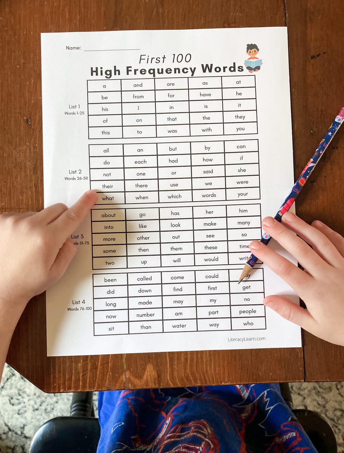 A child's hands pointing to the printed list of 100 High Frequency Words.