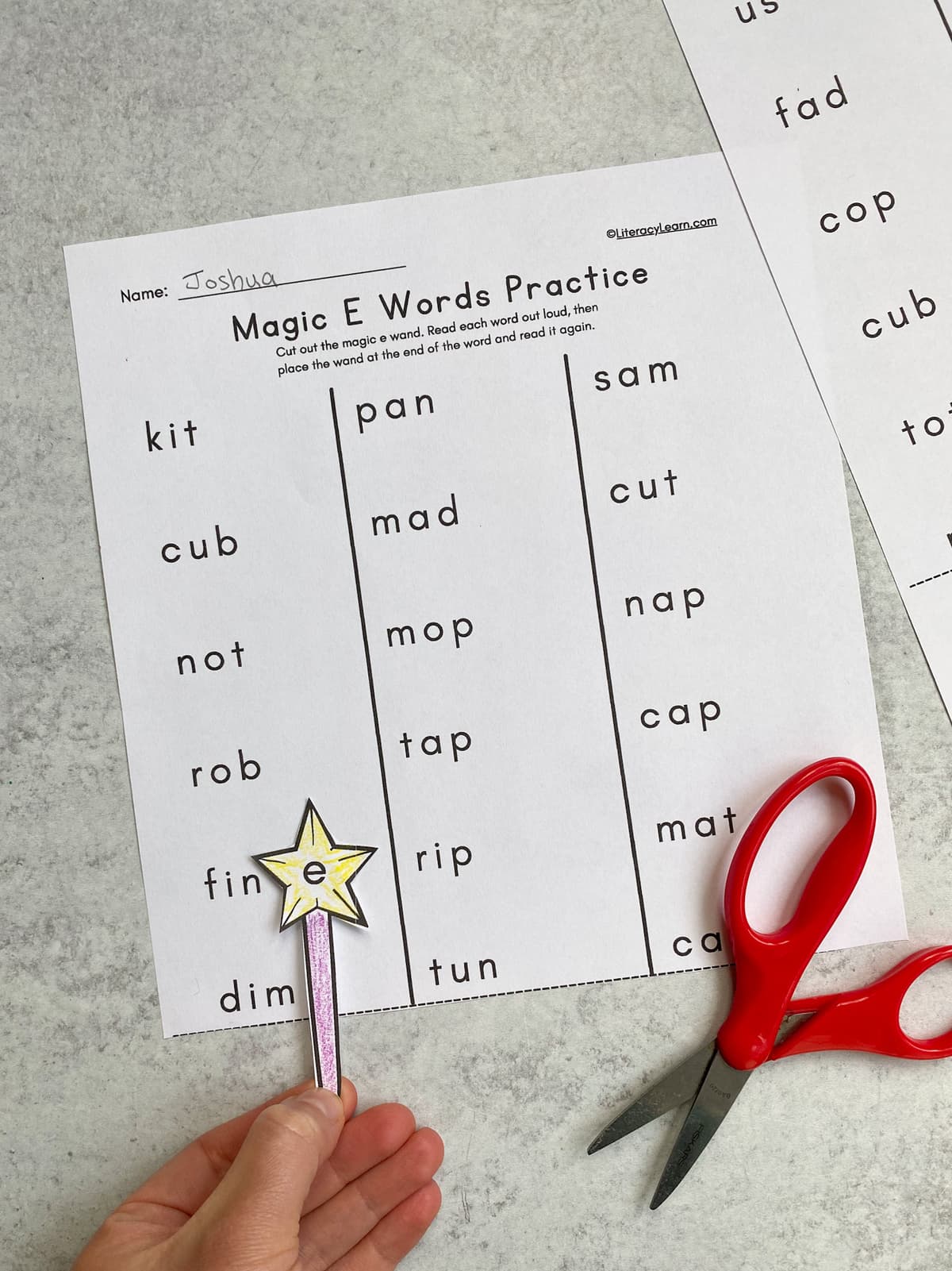 Close up of a hand holding the magic wand cutout on a silent e worksheet. 