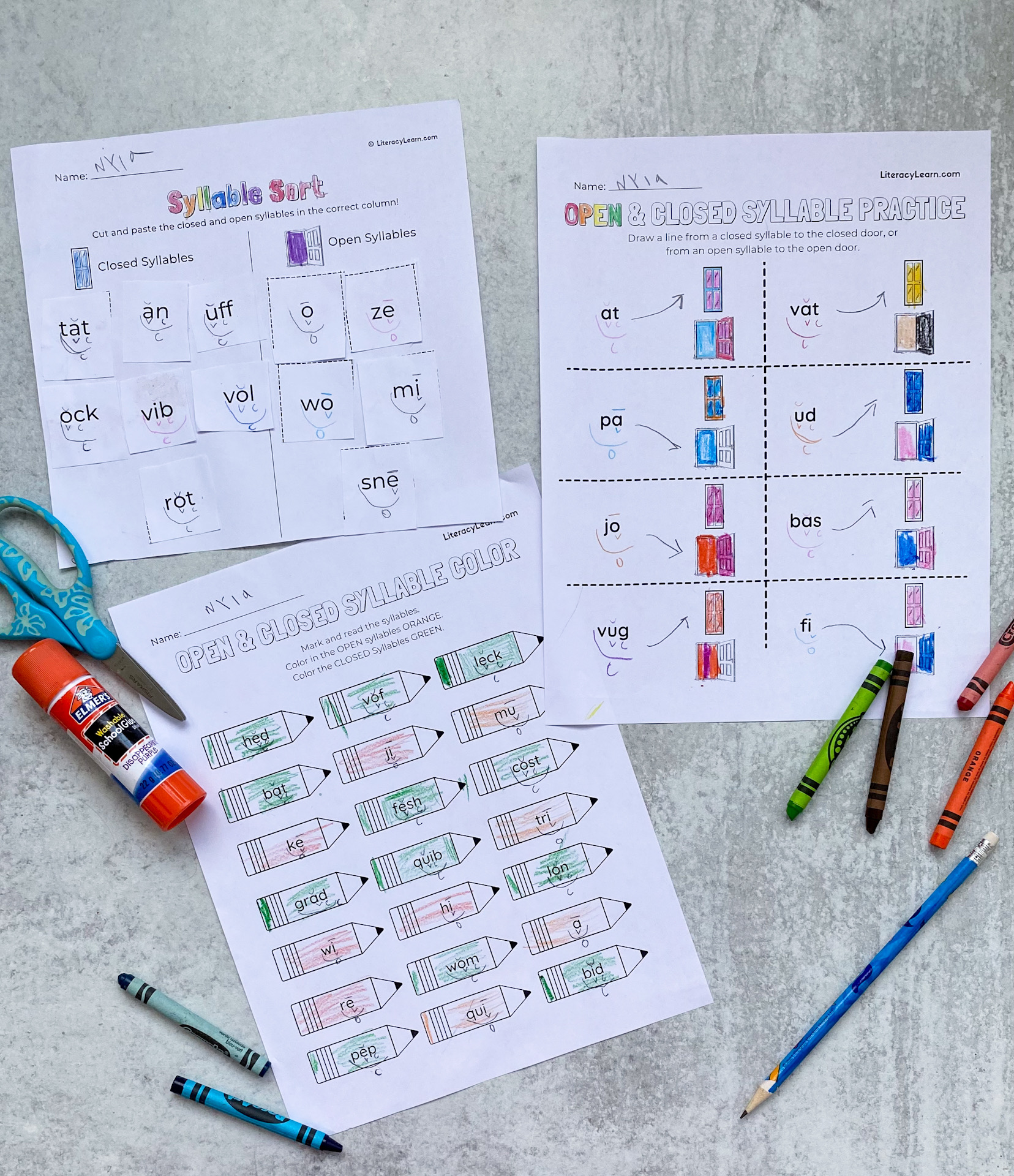 Three completed open and closed syllable worksheets with crayons, scissors, and a glue stick.