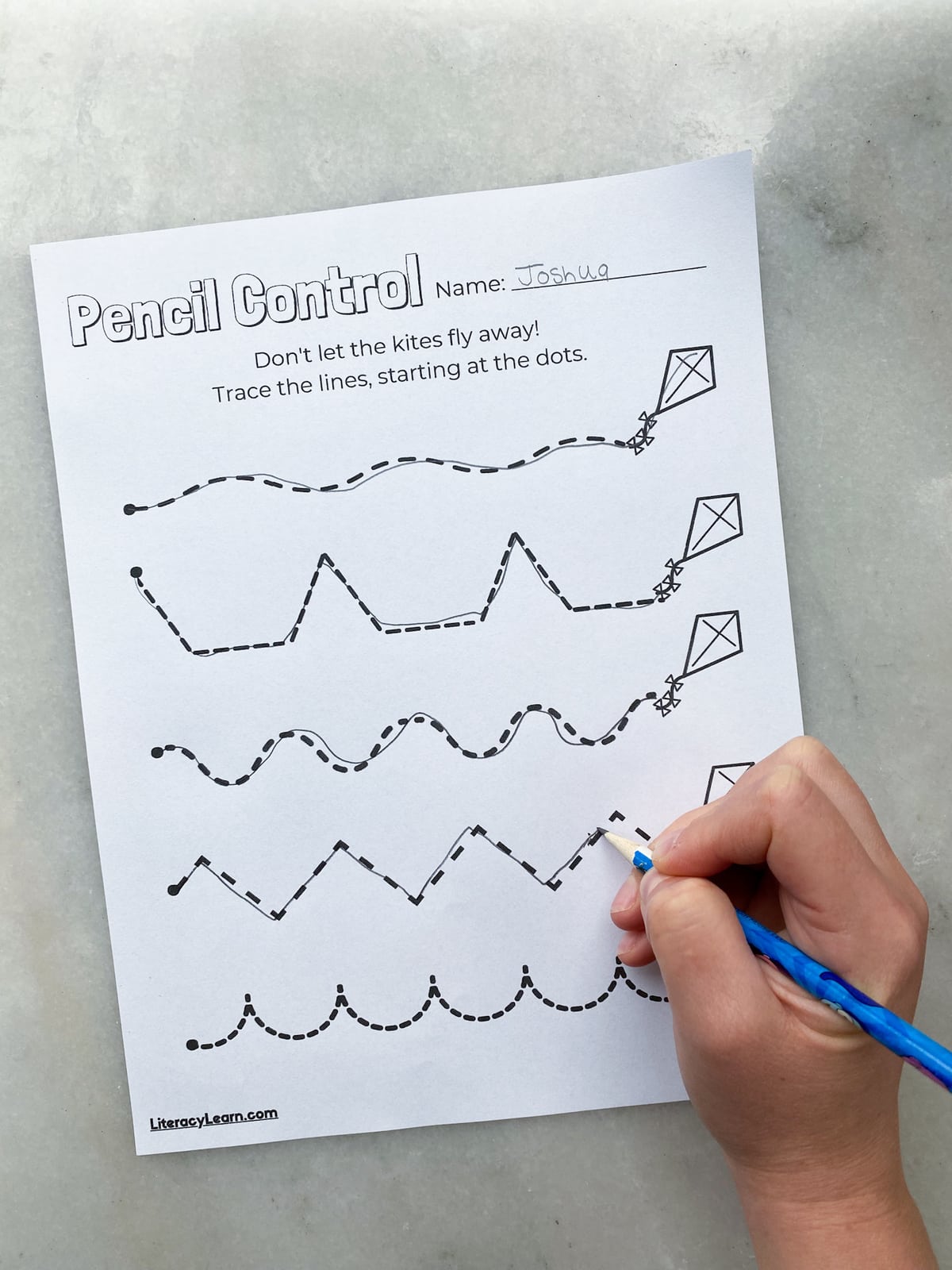 A child's hand tracing a pencil control worksheet featuring kite strings. 