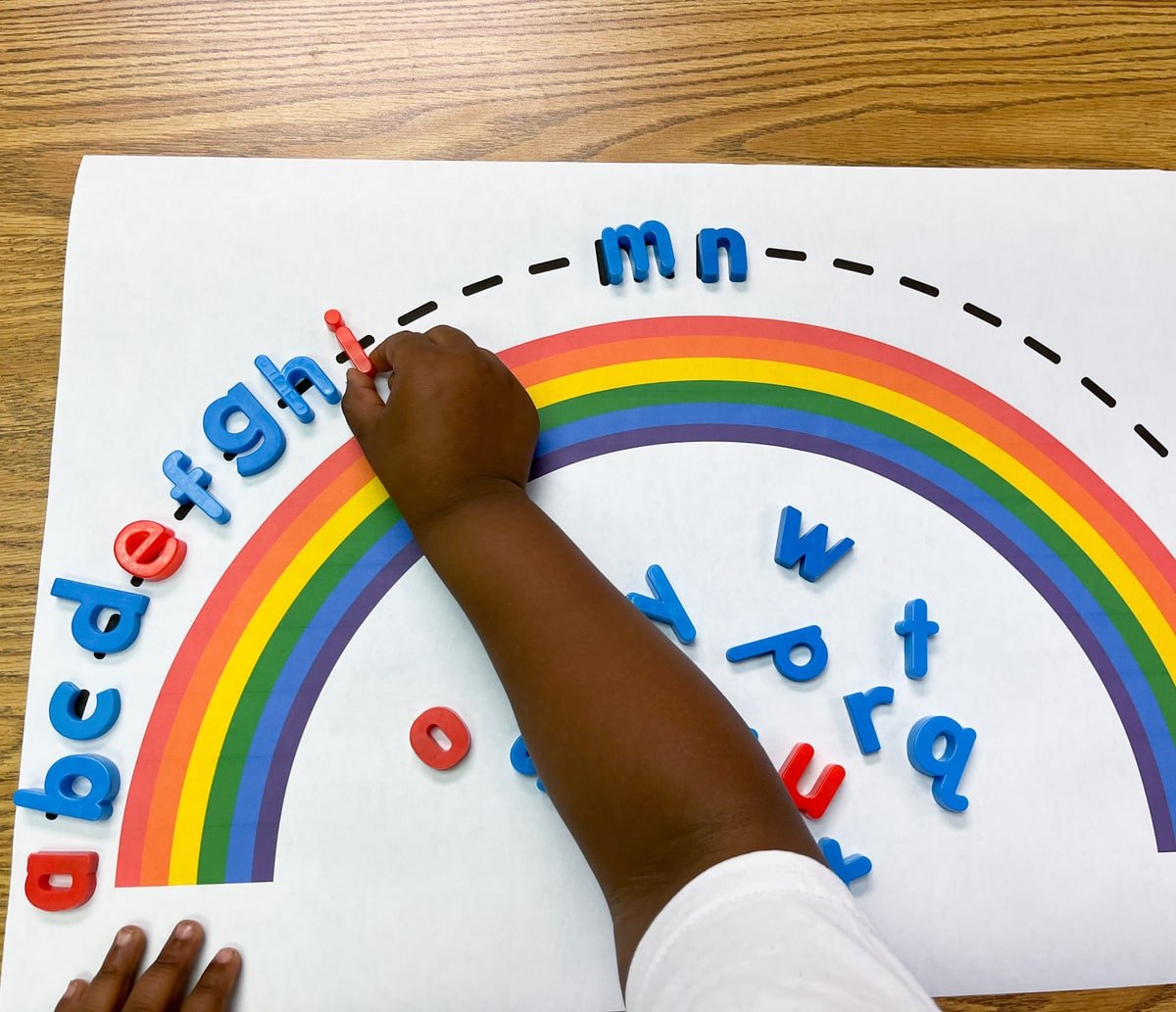 A child's hand touching magnetic letters on a partial alphabet arc.