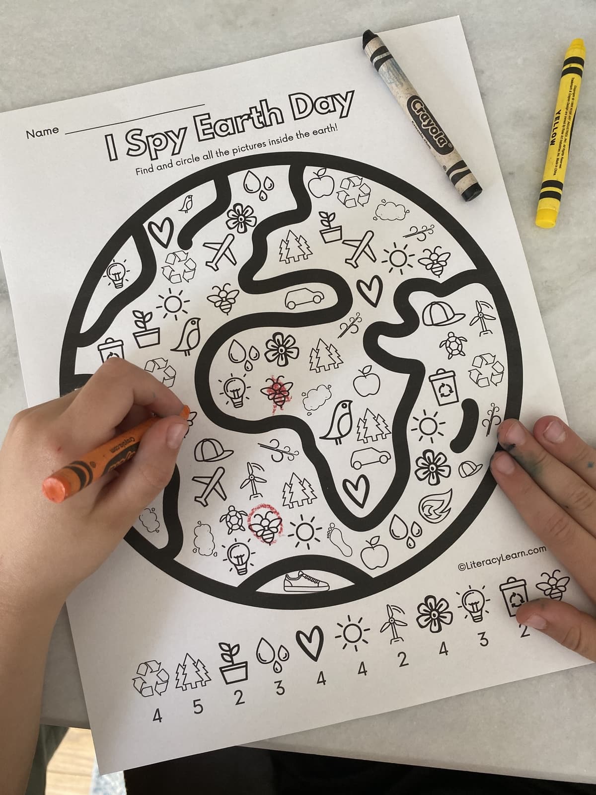 Close up of a child's hands coloring the I Spy Earth Day worksheet. 