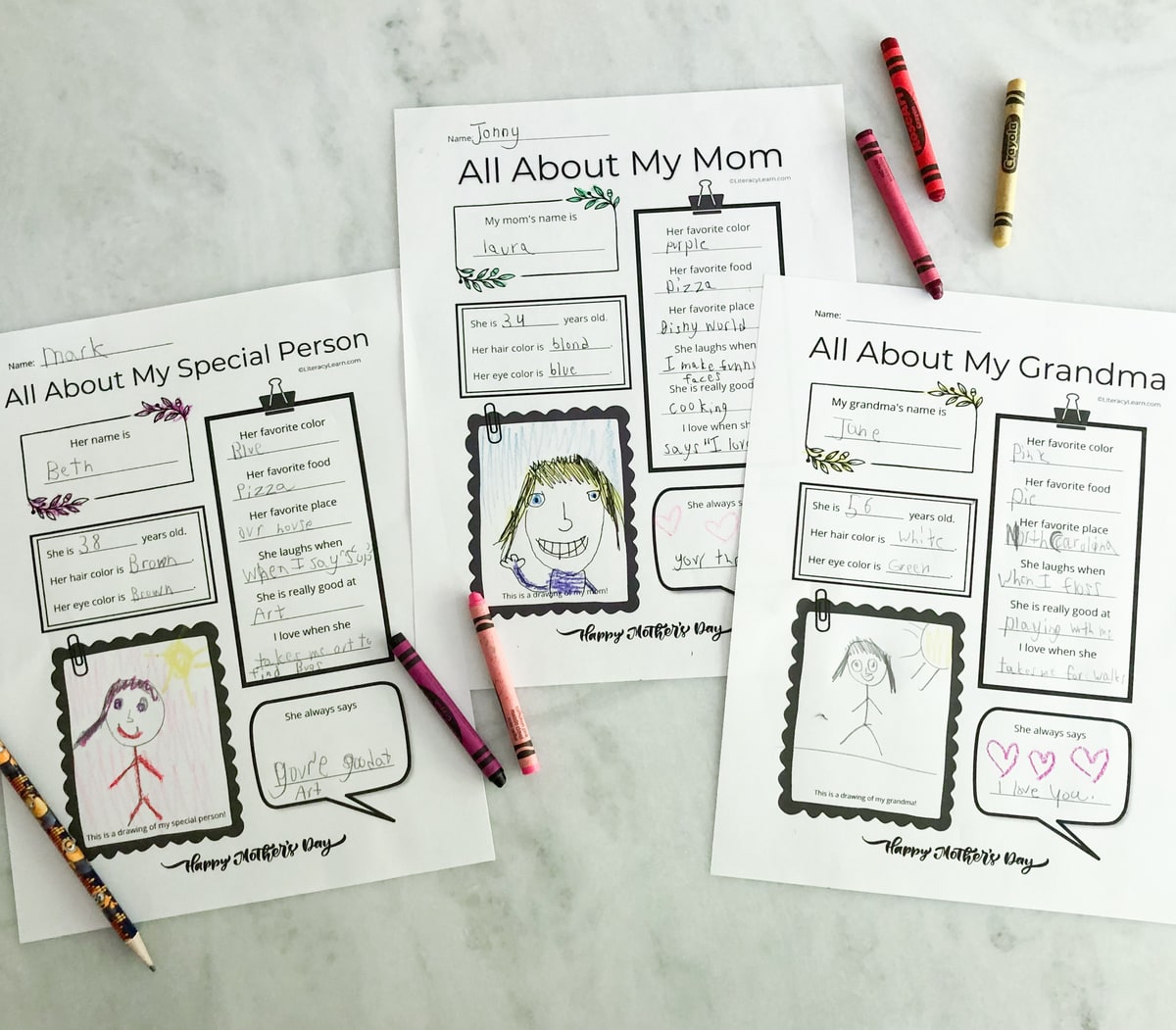 The three Mothers Day printables on a white marble board with crayons. 