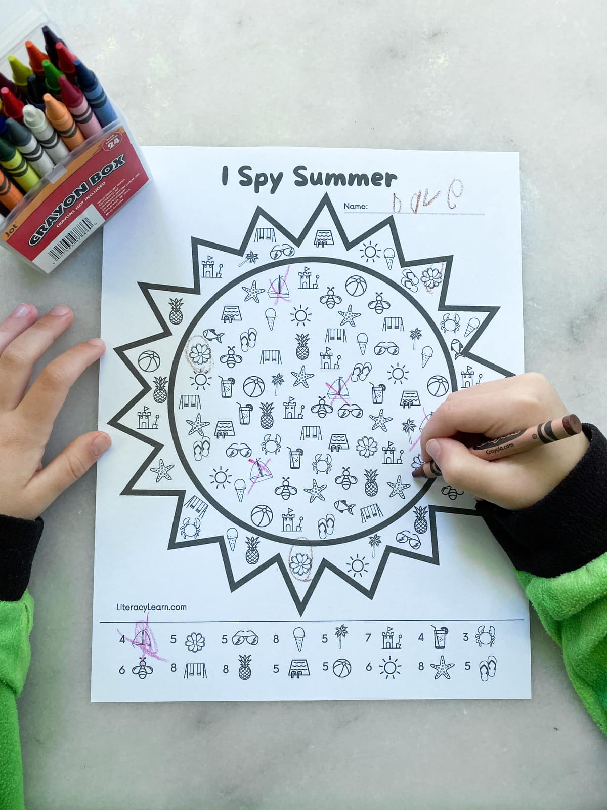 A child's hands completing the I Spy Summer worksheet with crayons.