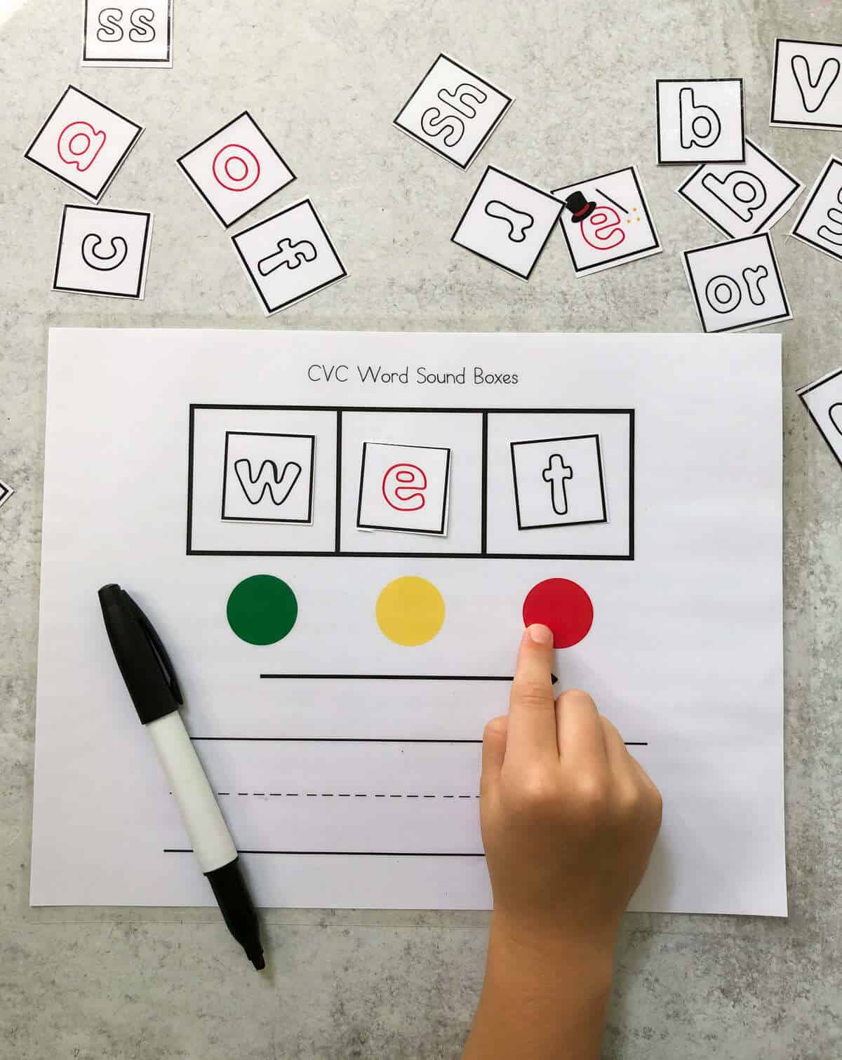 A child's hand mapping the word "wet" using sound boxes.