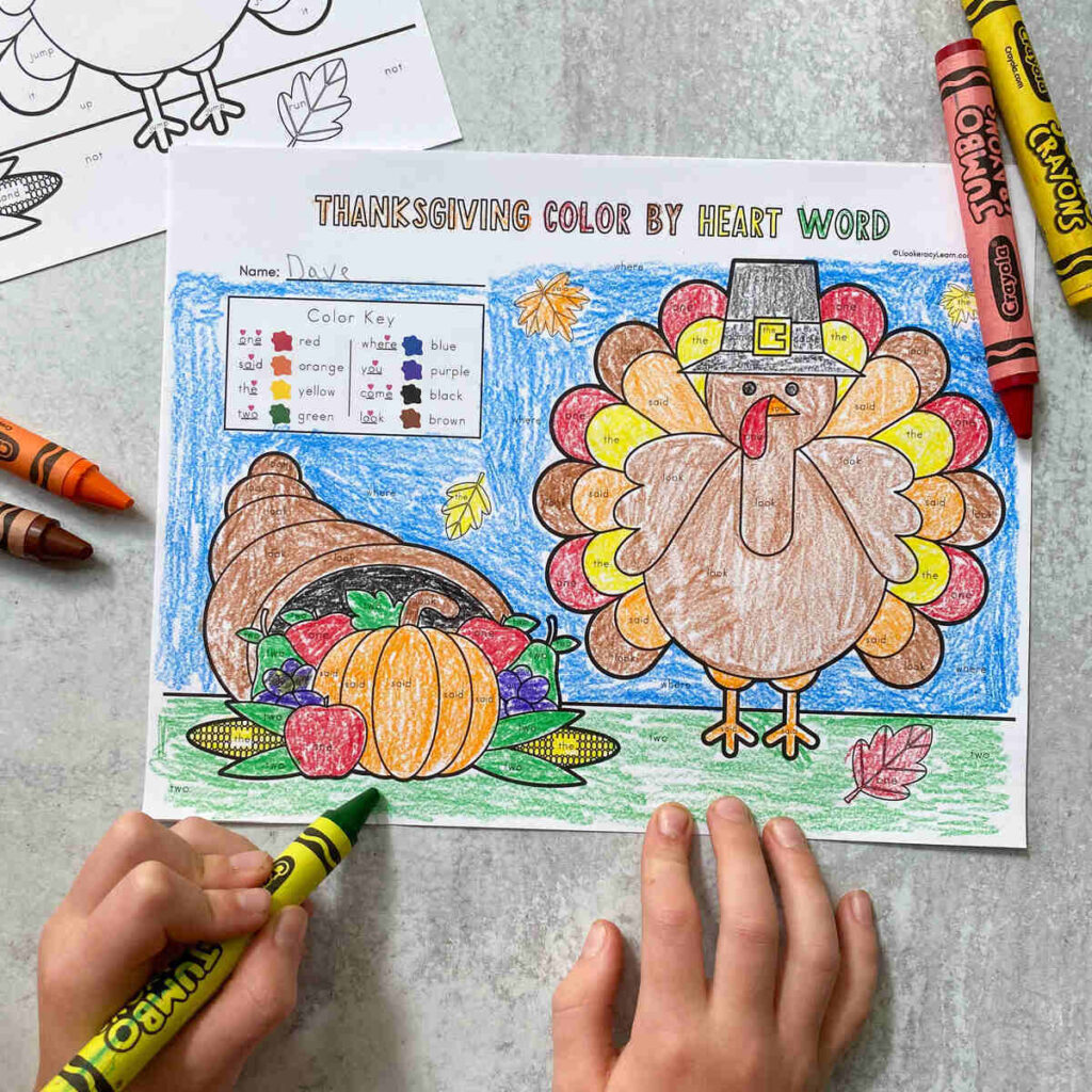 A child's hands coloring in a Thanksgiving themed color by sight word page.