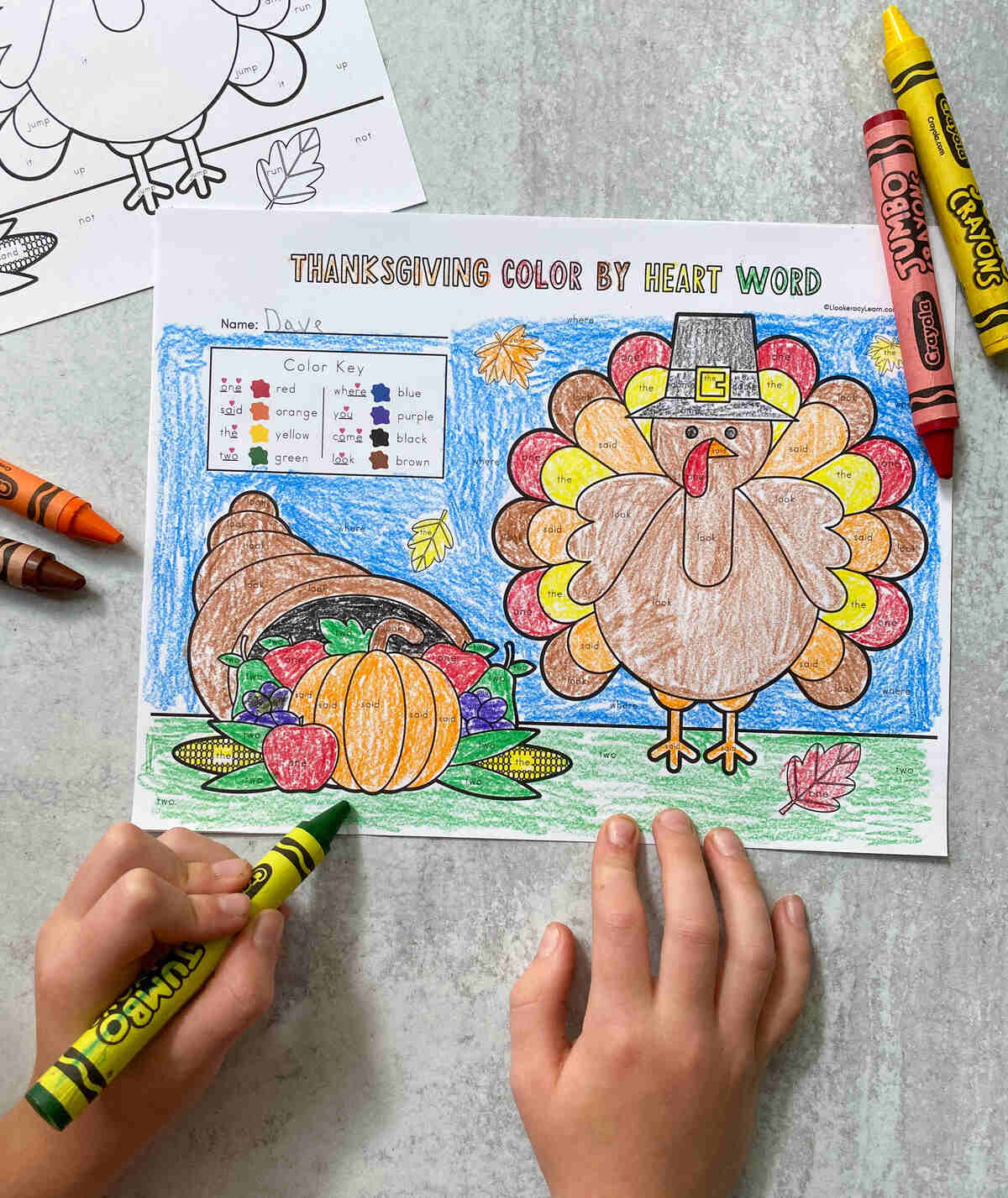 A child coloring in the Thanksgiving color by heart word printable. 