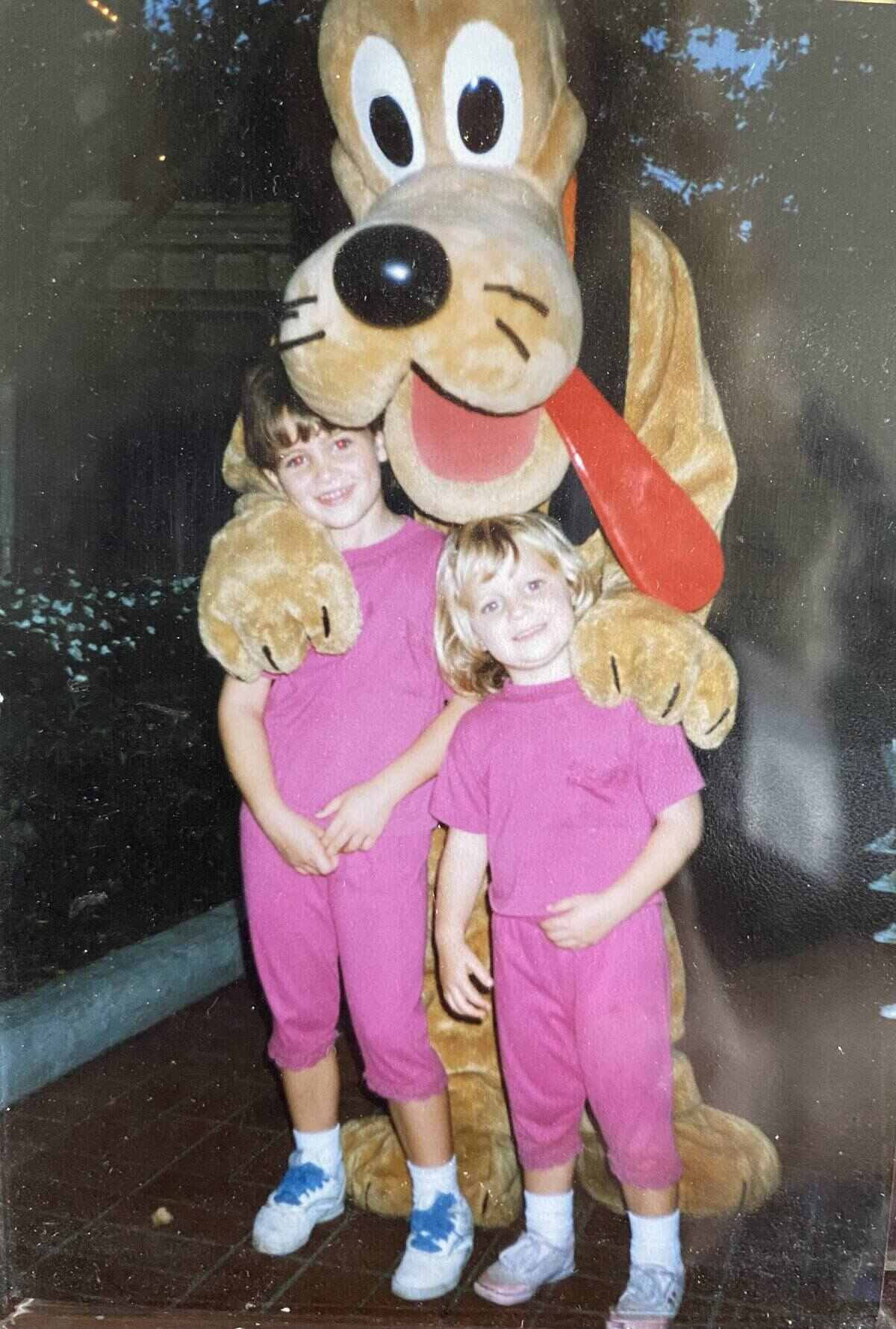 An old photo of two young girls posing with Goofy. 