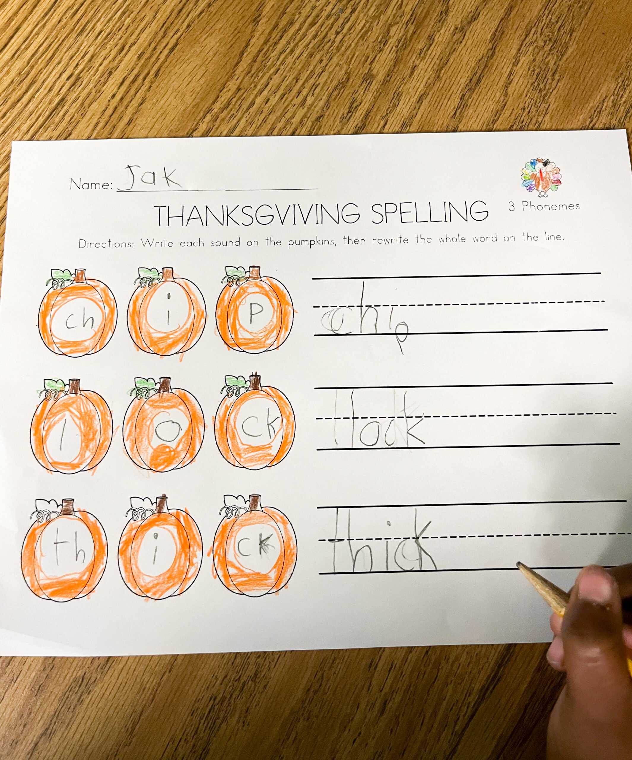 A child's hands writing words on the 3 phoneme word pumpkin mapping worksheet. 