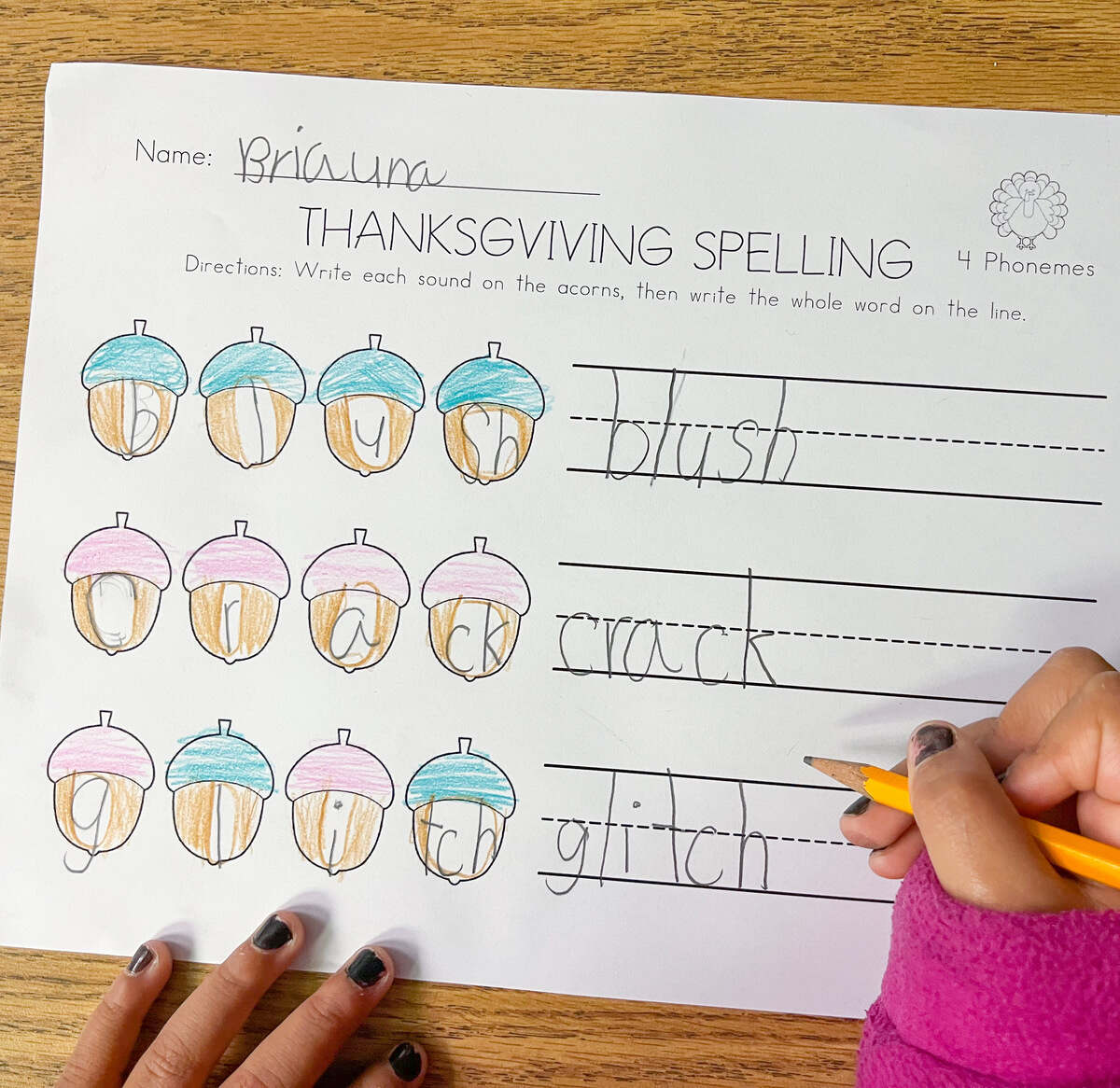 A child's hands writing words the 4 phoneme word mapping worksheet.