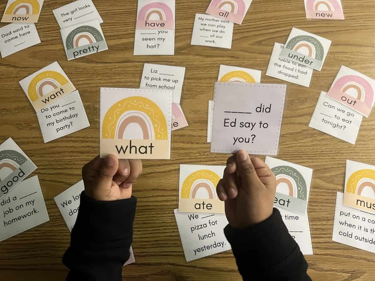 Student's hands holding the Dolch Word and sentence with game displayed in the background.