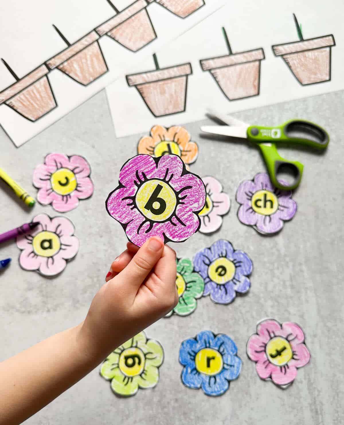 A child holding up a colored and cut out letter B flower. 