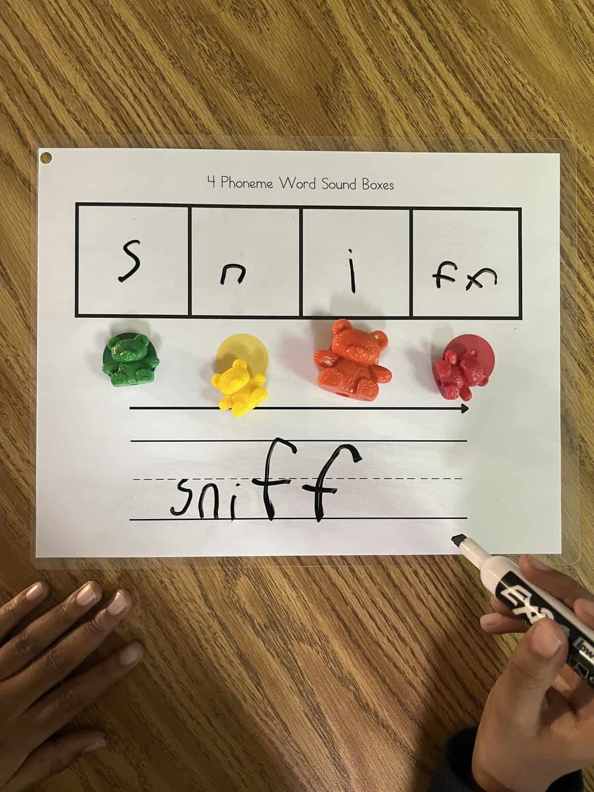 Photo of student's hands holding a marker using sound boxes to map the Floss word 'sniff.'
