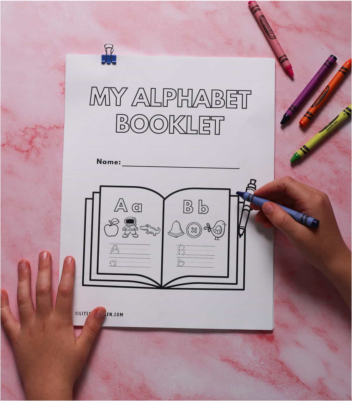 A child writing on the cover of the "My Alphabet Booklet" workbook.