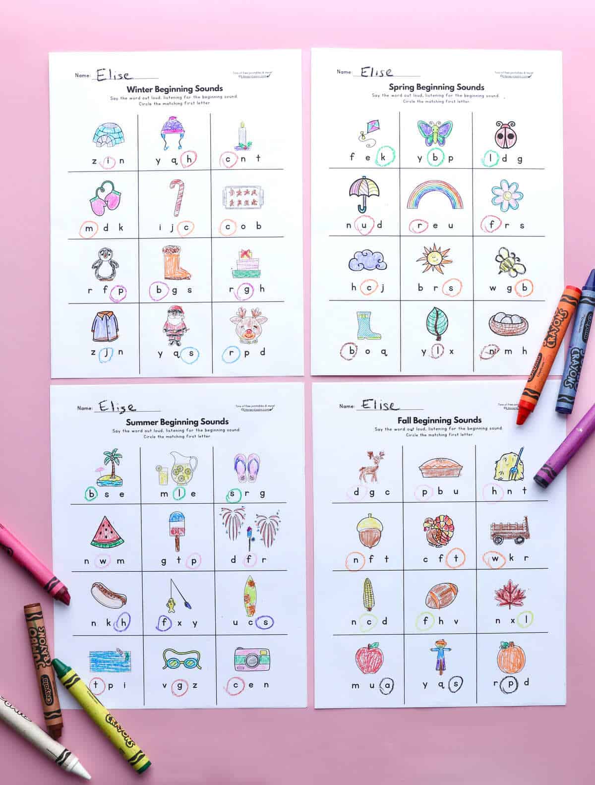 Four printed and completed initial sounds worksheets on a pink background with crayons.