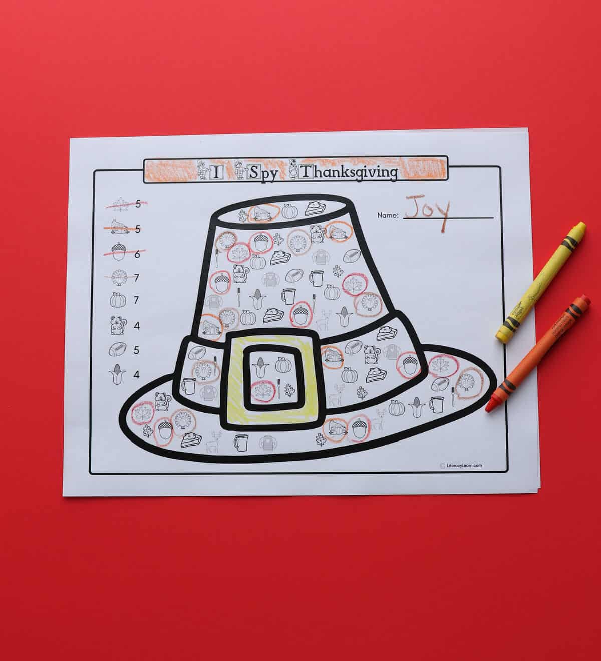 A printed I Spy Thanksgiving worksheet with crayons on a red background.