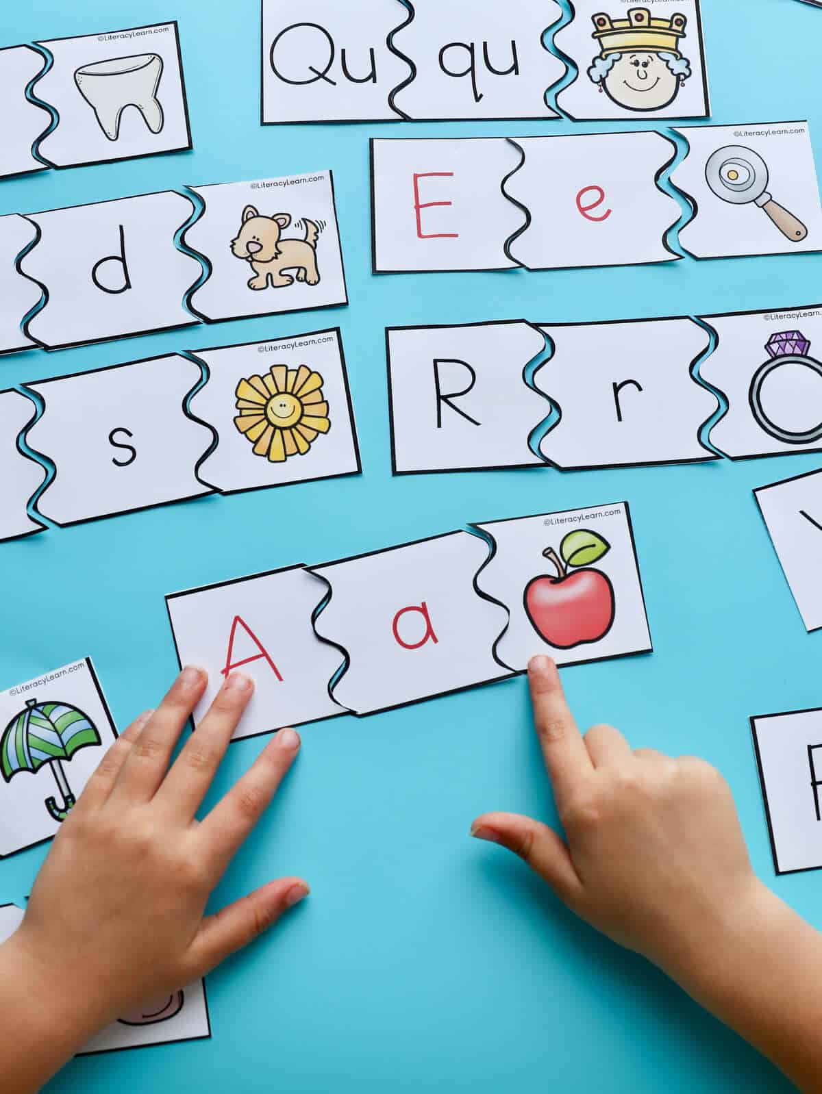 A child's hands matching the letter a with a picture of an apple.