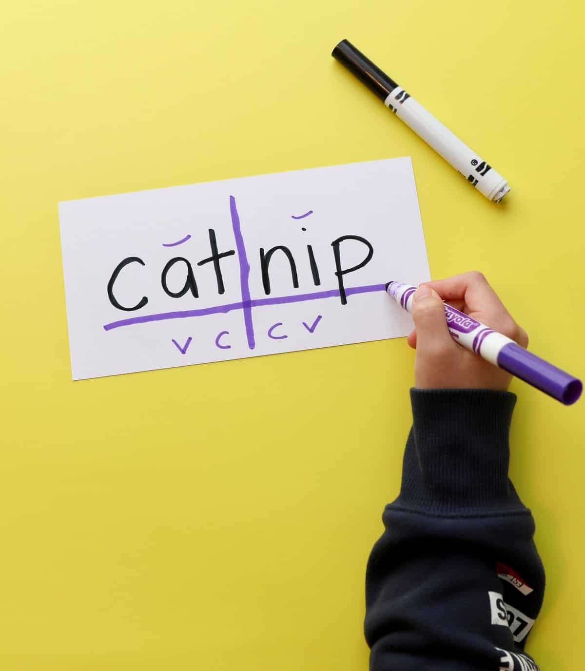 Photo of a child dividing syllables in the word 'catnip' following the syllable division rules poster.