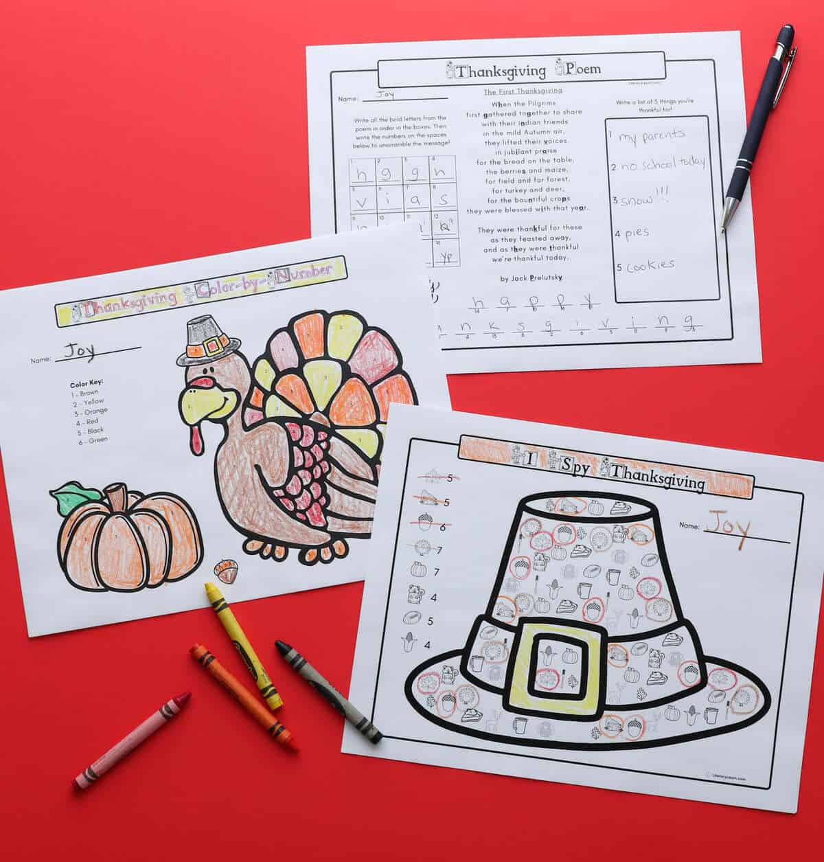 3 printed Thanksgiving themed activity placemats on a red board with crayons.