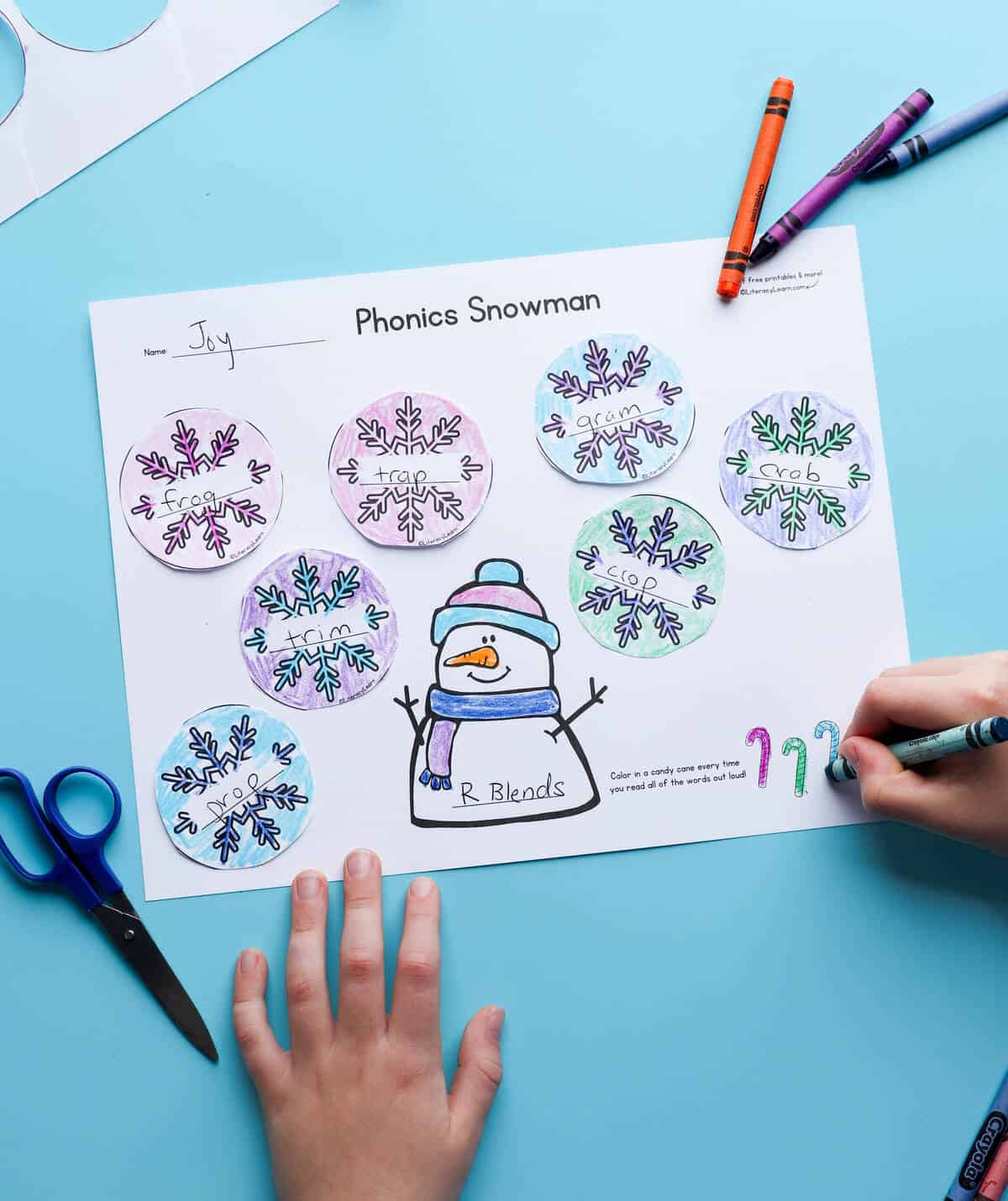 A child coloring on a printed and completed fluency snowman worksheet.