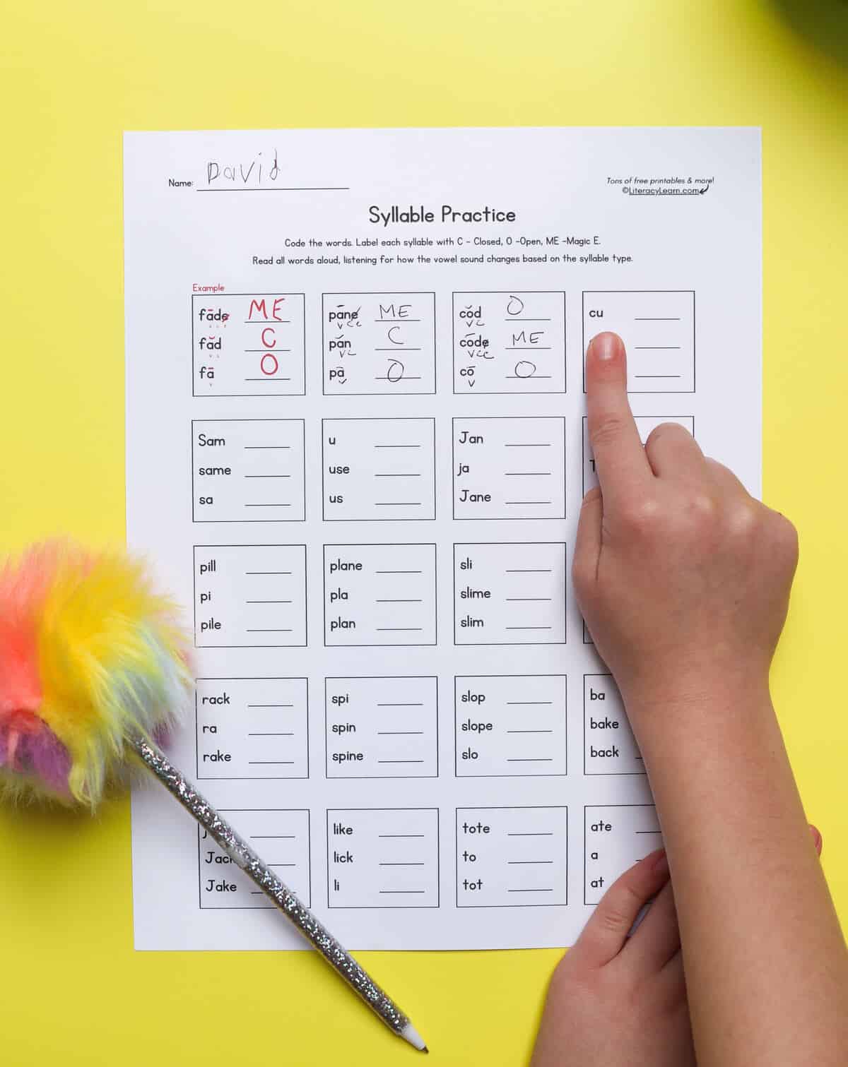 A child's hand pointing to words on the Magic e syllable type practice worksheet.