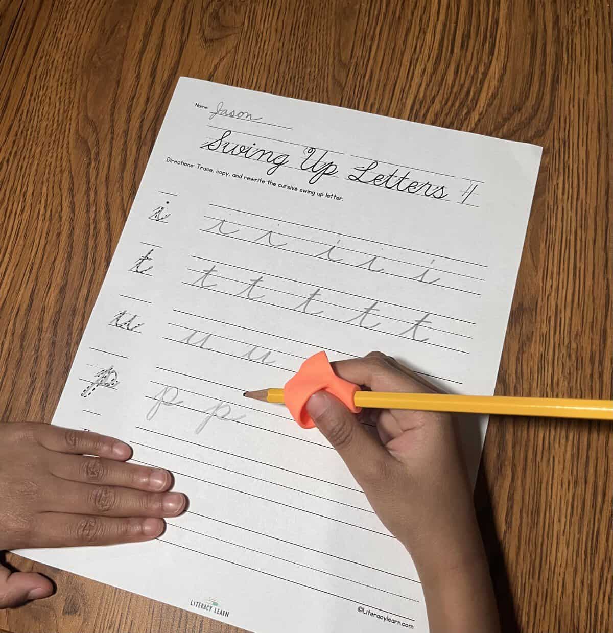 Photograph of students hands using a pencil grip completing a cursive writing worksheet.