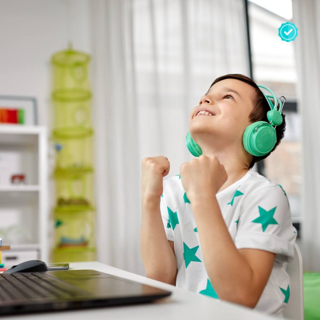 A child with headphones sitting at a laptop, smiling and celebrating.