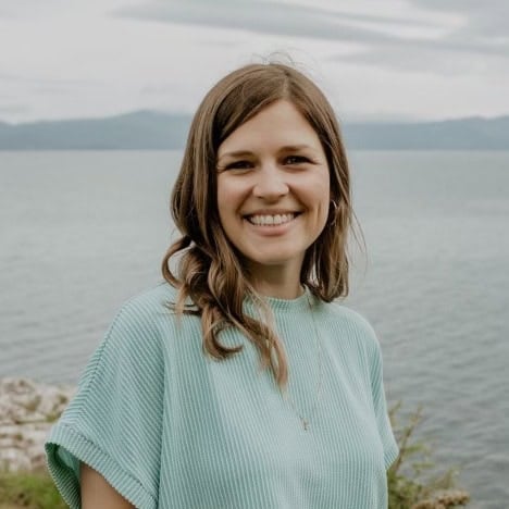 A smiling brown haired woman in front of the ocean.