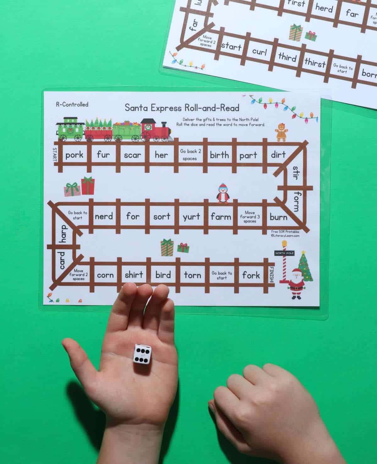 A printed R-Controlled game board with a child's hand rolling a dice.