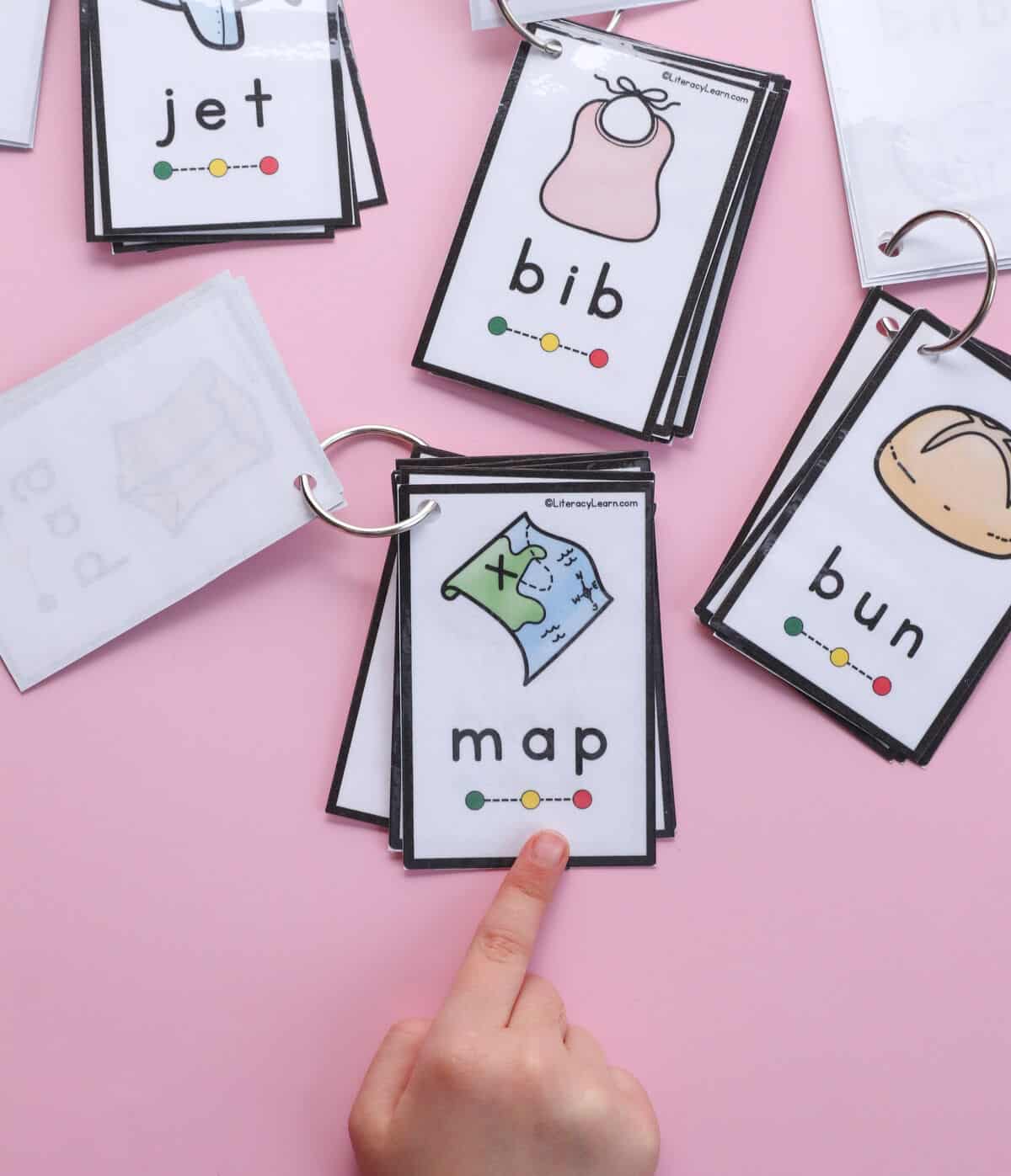 A child's hand pointing to the word "Map" on a CVC word and picture booklet card.