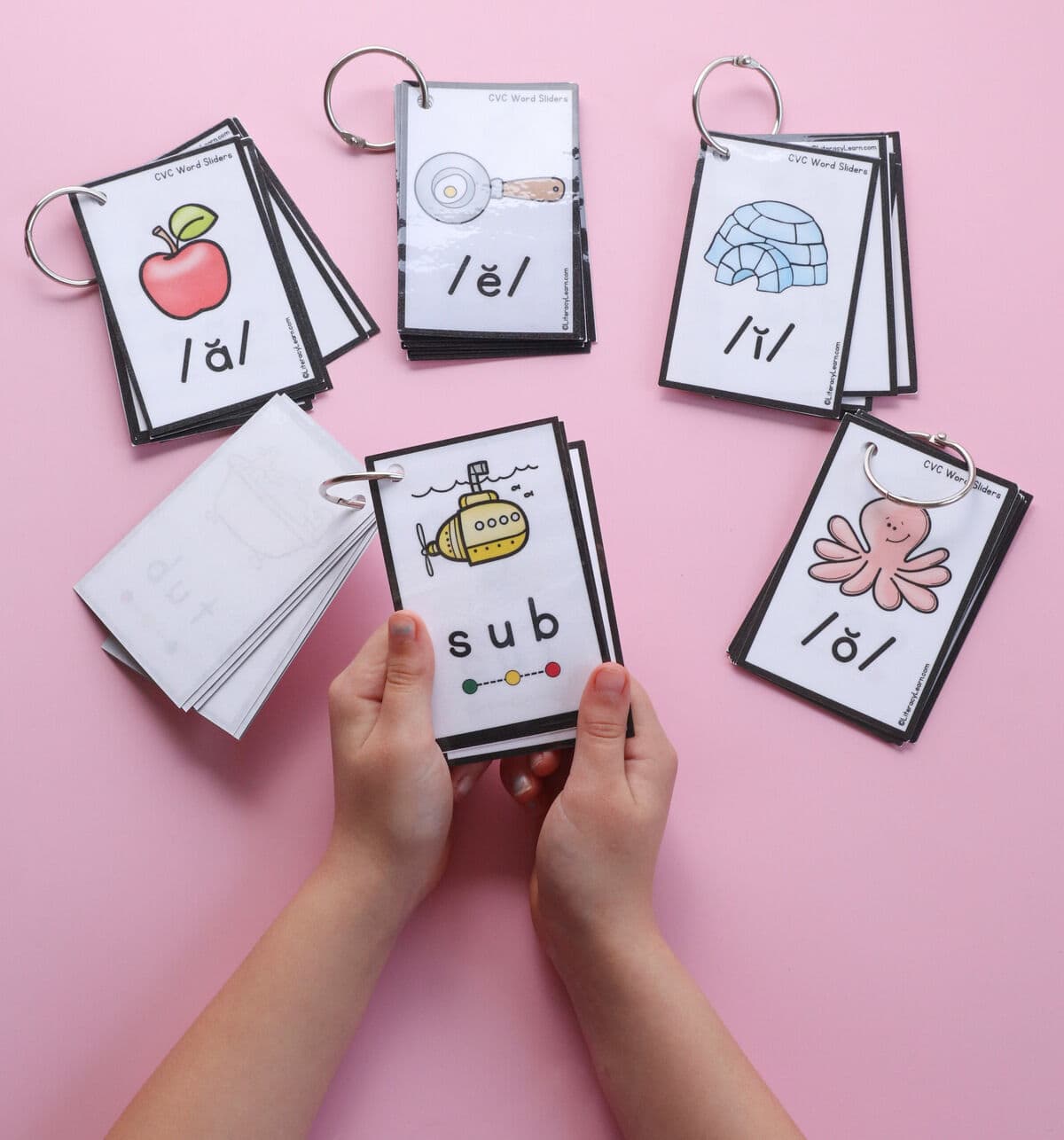 A child'd hands holding a CVC Word Slider booklet opened to the word "Sub."