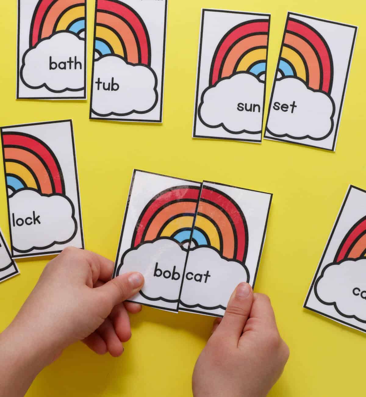 A child's hands matching rainbow puzzle pieces to make the compound word "bobcat."
