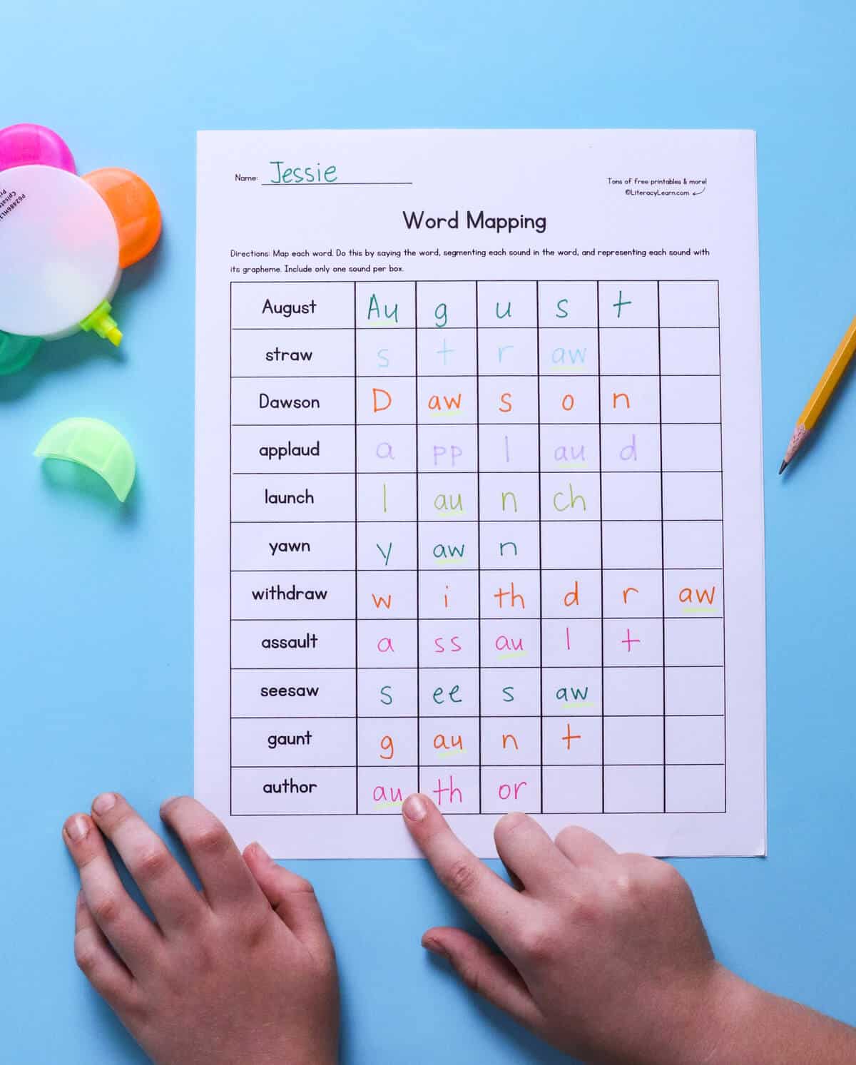 A child pointing to a word on a printed and completed au/aw word mapping worksheet.