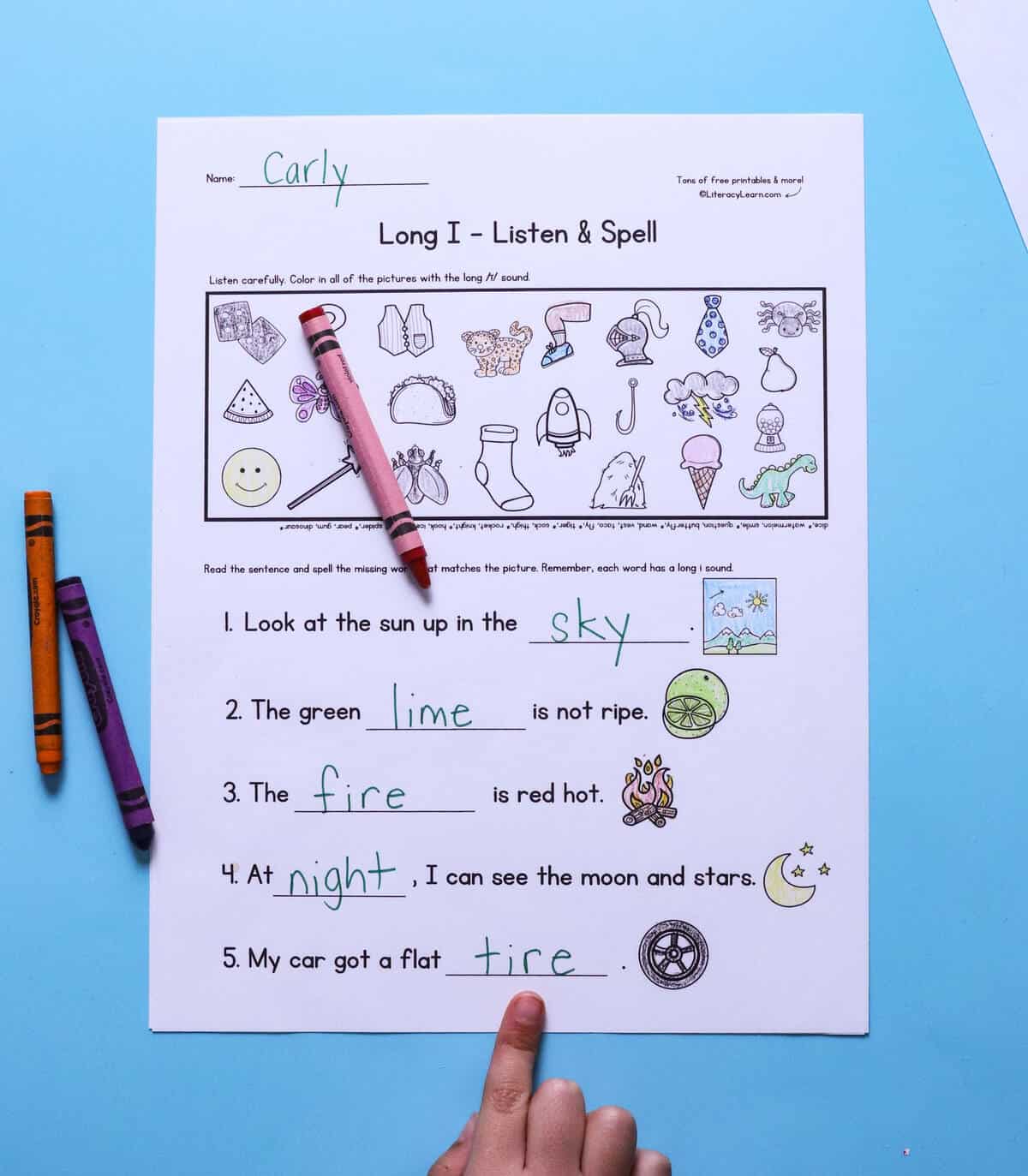 A child's hand pointing to a printed and completed long I listen & spell worksheet.