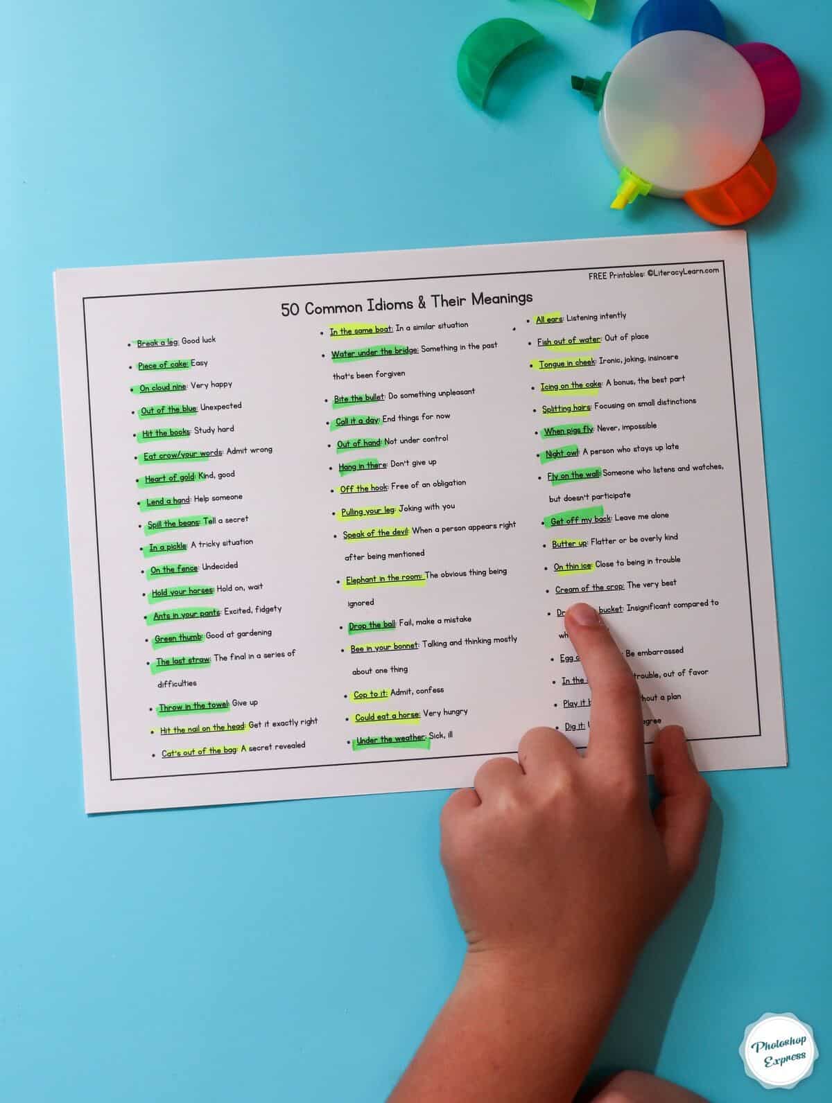 A child's hand pointing to a printed list of 50 common idioms.