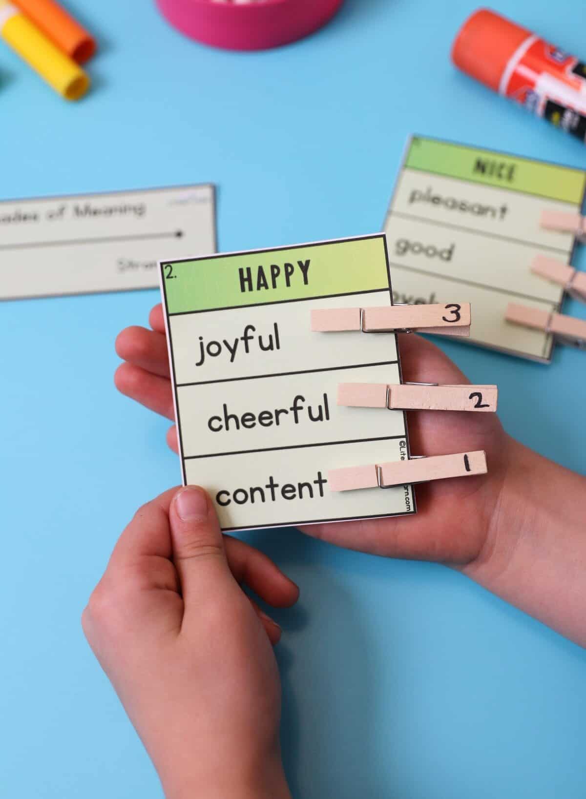 A child's hands holding the "Happy" semantic gradient card with numbered clothes pins.