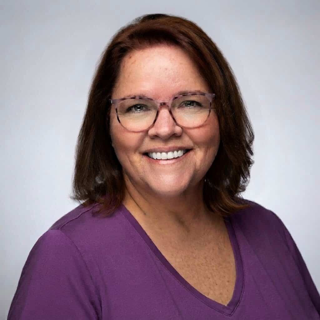 A smiling brown haired woman in glasses.